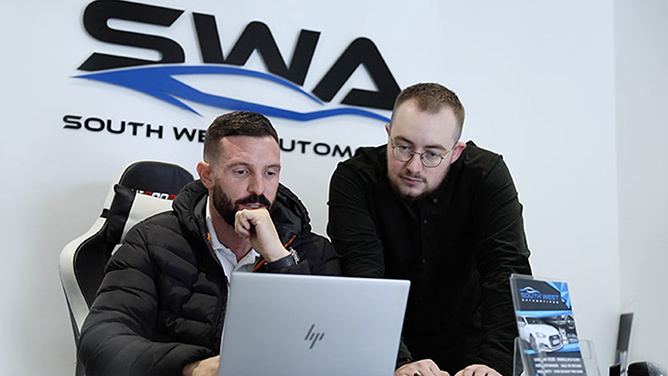 A car dealer and advisor look at a laptop